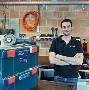 Een man in een zwart shirt staat voor blauwe Bosch gereedschapskisten.