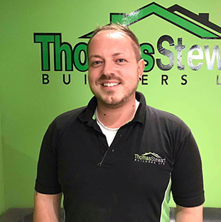A man smiles in front of a green wall with a "Thomas Stewart" logo.