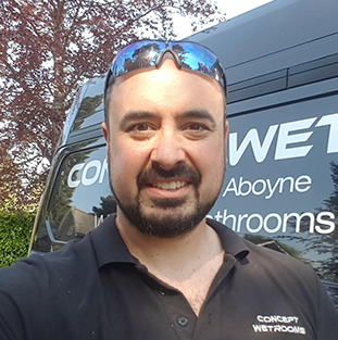 A man in a black shirt smiles in front of a delivery van with a logo.