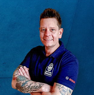Ein lächelnder Mann mit Tattoos trägt ein blaues Bosch Professional Polo.
