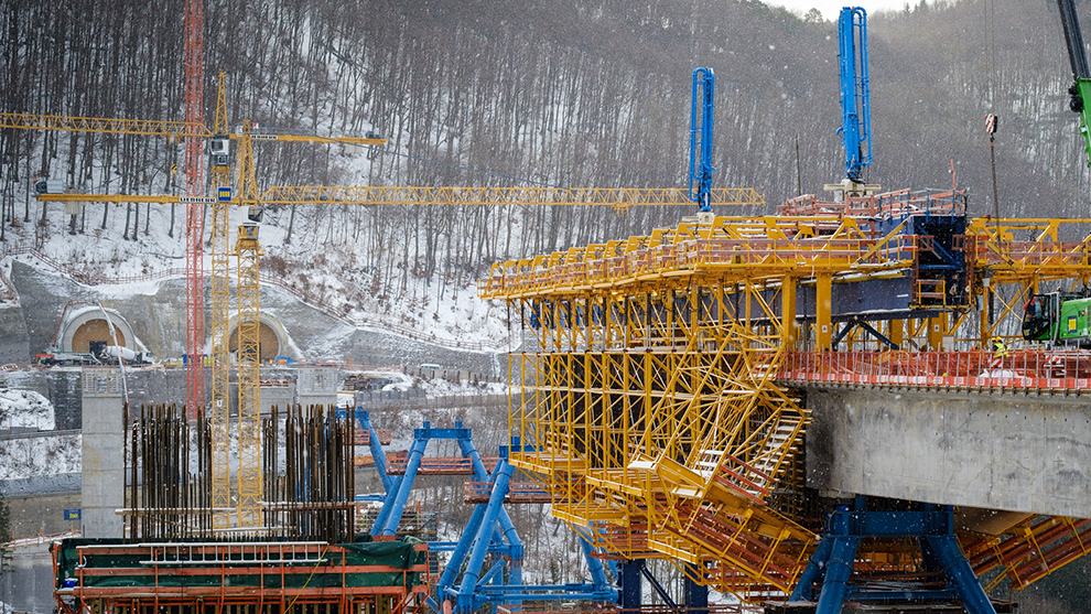 Byggarbete med kranar, räcken och betong på en byggarbetsplats i snön.