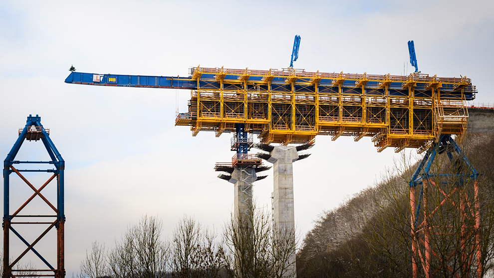 En gul konstruktion svävar över två grå betongpelare.