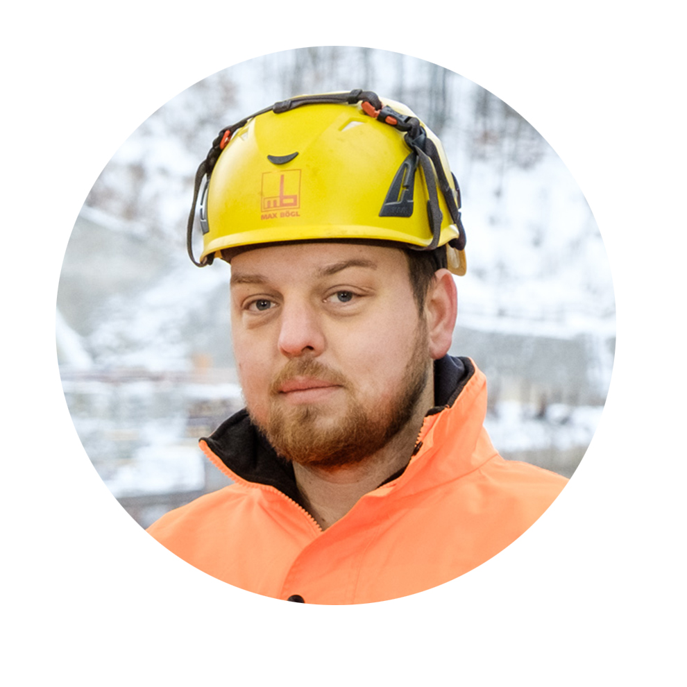 En man med gul hjälm och orange jacka tittar in i kameran.