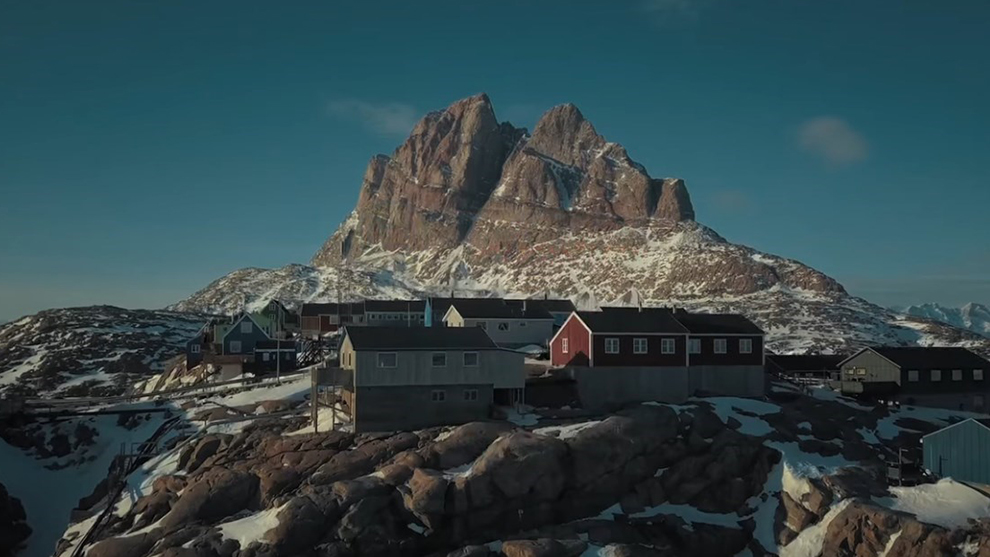 Bunte Häuser stehen unter einem großen Felsen in schneebedeckter Landschaft.