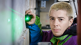 Ein junger Mann mit blonden Haaren benutzt einen grünen Laser auf einer Wand.