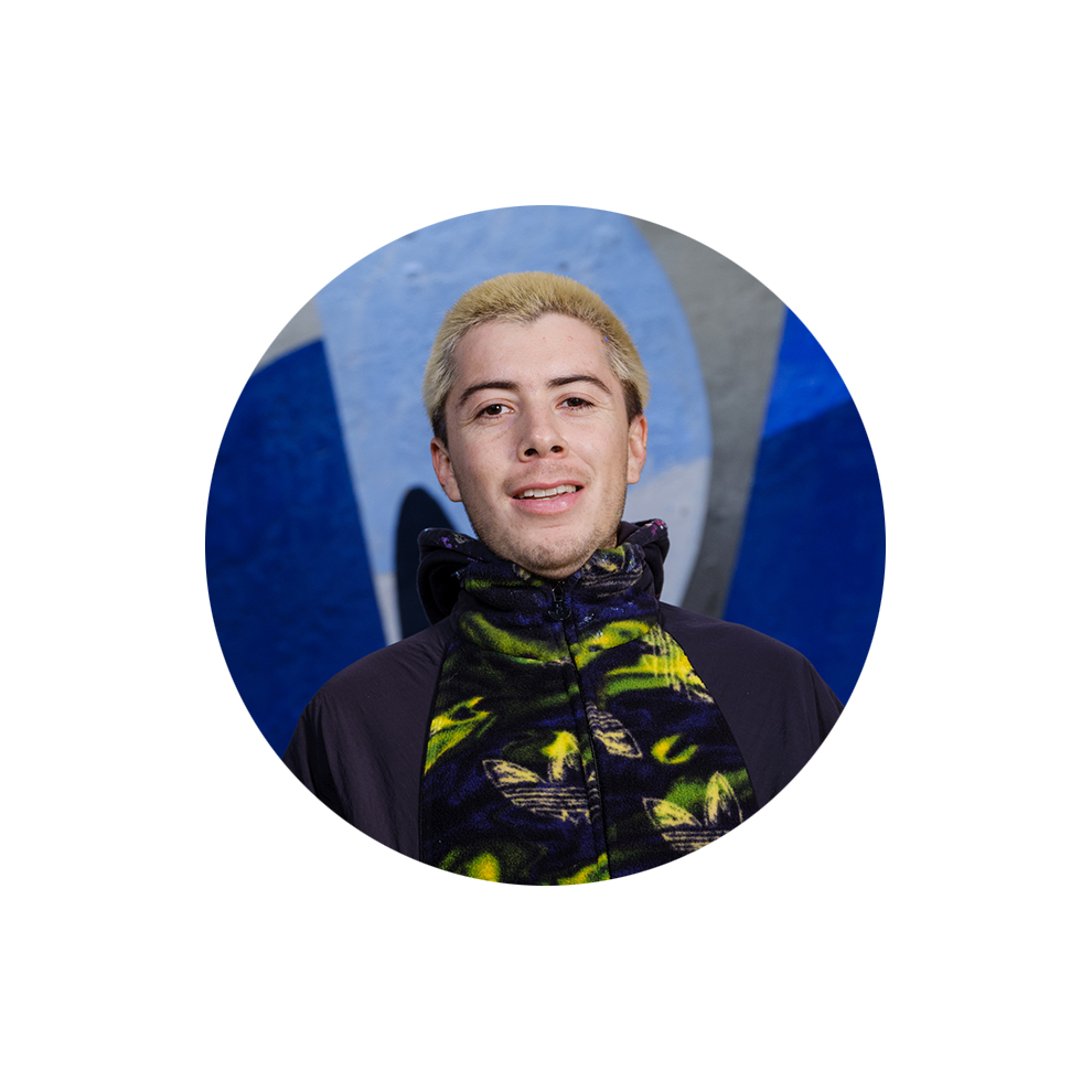 Noor mees, kellel on blondid juuksed ja värviline kapuuts, seina taustal.