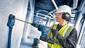 Um homem com capacete de segurança está perfurando com uma furadeira sem fio azul da Bosch Professional.
