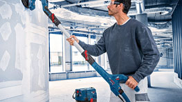 En hantverkare använder en blå Bosch Professional slipmaskin på en vägg.