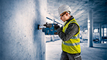 En arbetare med hjälm och varselväst borrar i en betongvägg.