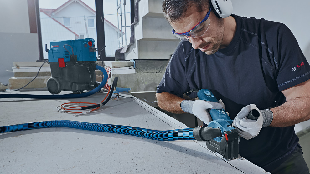 Mężczyzna używa niebieskiego narzędzia Bosch Professional przy stole.