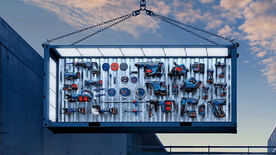 Eine große, beleuchtete Werkzeugwand mit verschiedenen Bosch Professional Werkzeugen in Blau und Rot, hängt an Ketten in einem urbanen Umfeld. Die Werkzeuge sind ordentlich angeordnet, darunter Bohrmaschinen, Sägen und Schleifgeräte, vor einem klaren Himmel.