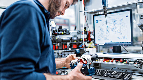 Ein Mann in einem blauen Hemd hält zwei Werkzeuge und betrachtet einen Computerbildschirm.
