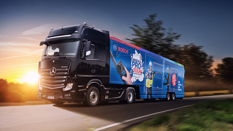 Schwarzer Mercedes Lkw mit Bosch-Profi-Tour-Werbung fährt bei Sonnenuntergang.