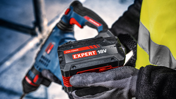 Pracovník drží černou baterii s červeným nápisem "EXPERT 18V" v ruce.