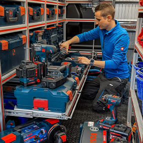 Ein Mann in blauer Jacke arbeitet in einem Werkzeugwagen, umgeben von Bosch Professional Werkzeugen in Blau und Rot.