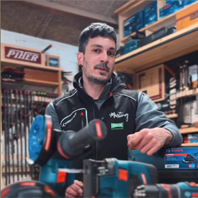 Un hombre con chaqueta de trabajo negra está sentado frente a herramientas de Bosch Professional en un taller.