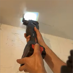 Una persona sostiene un amoladora angular inalámbrica Bosch Professional negra, apuntando hacia el techo. Una luz está encendida.
