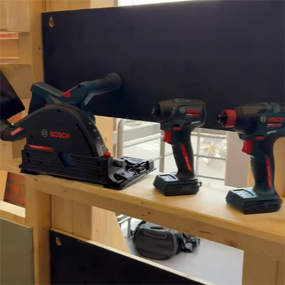 Une scie circulaire Bosch Professional est posée sur une étagère, flanquée de deux visseuses sans fil en noir et rouge.