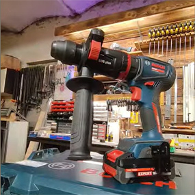 Un trapano avvitatore a batteria Bosch Professional blu è posato su un tavolo da lavoro, circondato da attrezzi.