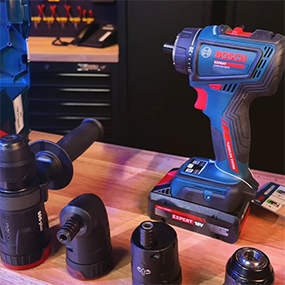 Un avvitatore a batteria Bosch Professional blu è posato su una superficie di legno, circondato da vari accessori.
