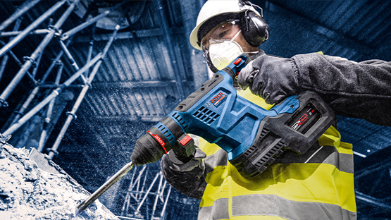 Робітник у касці використовує синю дрель Bosch на будівельному майданчику.