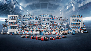 Několik polic s modrými nástroji v průmyslové hale, včetně strojů a příslušenství.