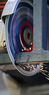 Ringsaag lõikab läbi halli materjali, lõikepinnalt lendavad sädemed.