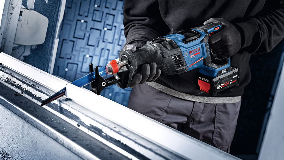 Inimene, kellel on seljas must sviiter ja kindad, hoiab Bosch saagi ja lõikab metallprofiili.