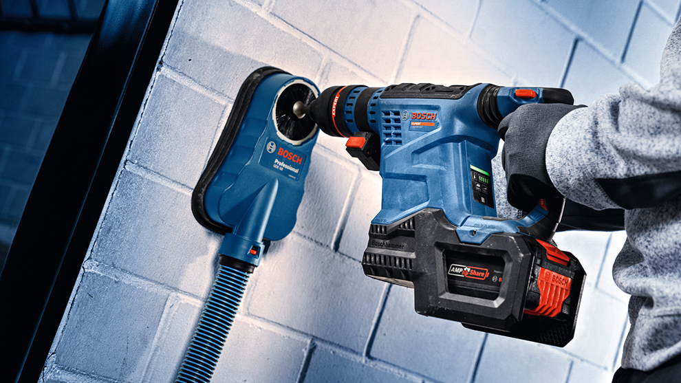 Inimene kasutab heledal seinal sinist Bosch akutrelli. Tolmuimeja on ühendatud.