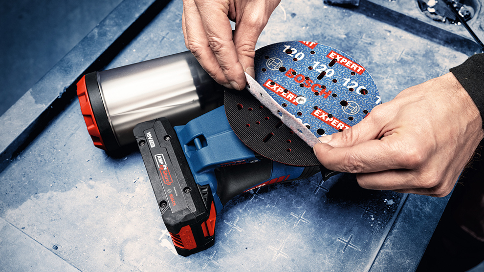 Käsitööline vahetab sinise akkusiluri lihvpinda tööpingil.