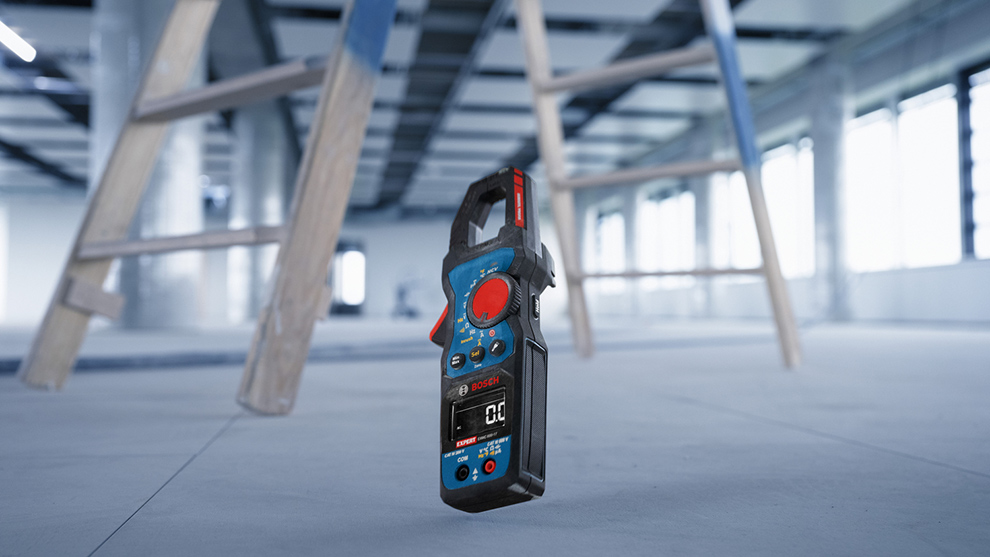 Sinine mõõteseade Bosch seisab heledal põrandal, taustal puidust redel.