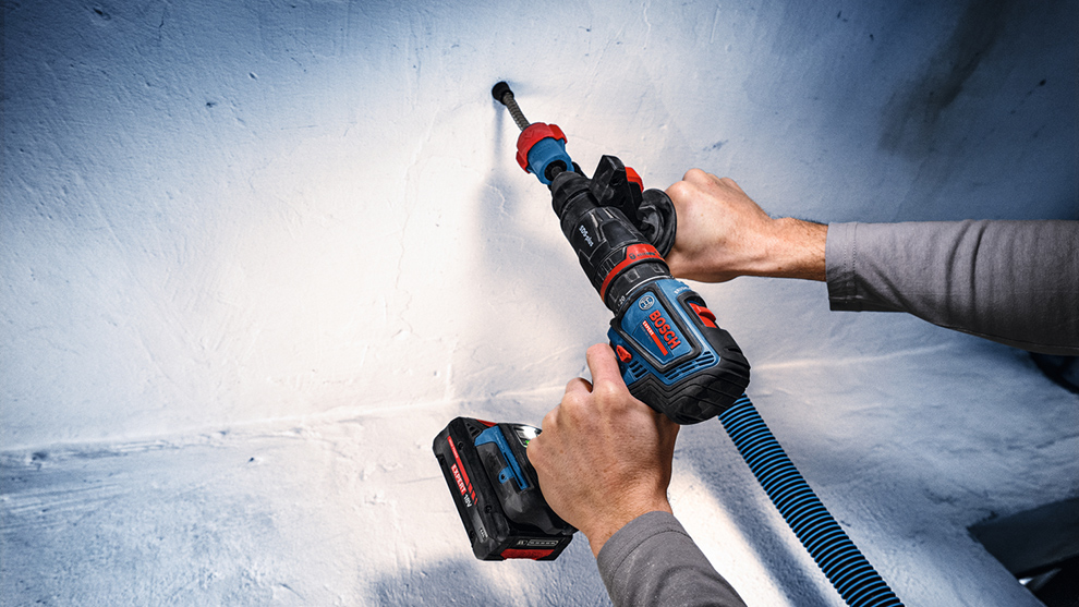 A person uses a cordless drill in blue and red to drill into a white wall.