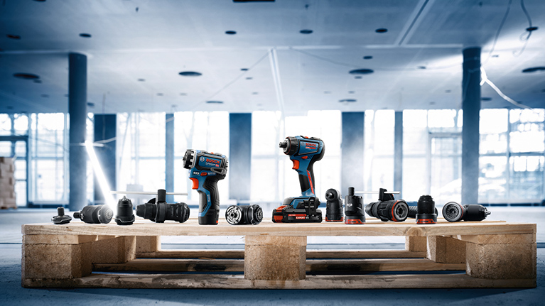 A wooden pallet with various tools, including a cordless drill and attachments, on a construction site floor.