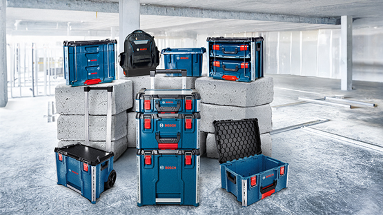 Several Bosch Professional toolboxes in blue and black are arranged on gray building blocks. A backpack is placed on top.