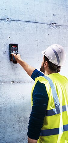 Um homem com colete de segurança amarelo e capacete utiliza um equipamento Bosch Professional em uma parede de concreto.