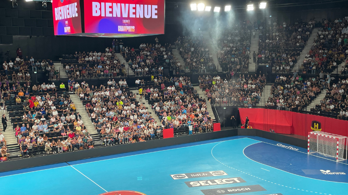 Un grand nombre de spectateurs dans un stade de sport, match de handball en cours.