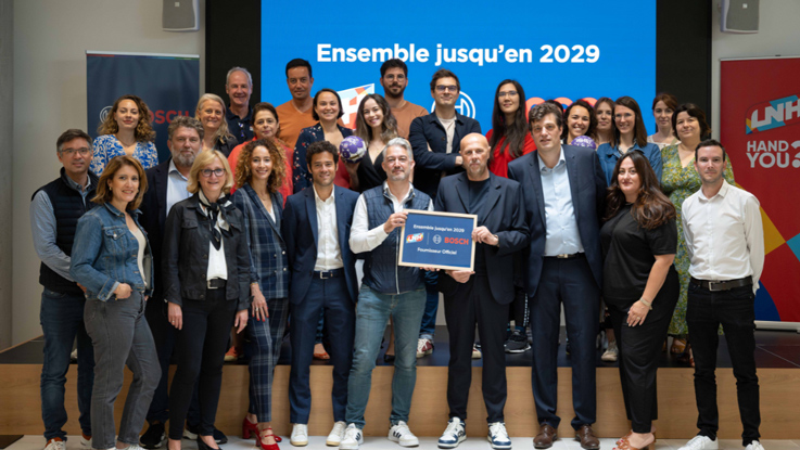 Un groupe de personnes pose devant un mur de présentation avec des logos.