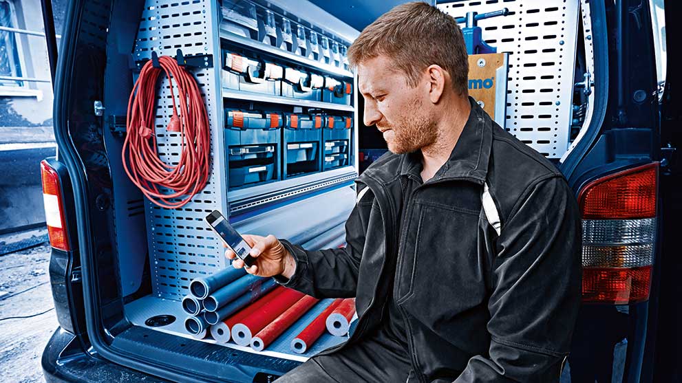 Mustas riietuses käsitööline istub vanis ja vaatab oma telefoni.