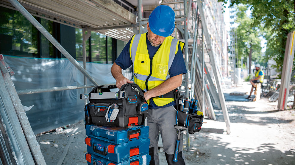 Būvstrādnieks ar zilu ķiveri strādā pie Bosch rīku kastes.