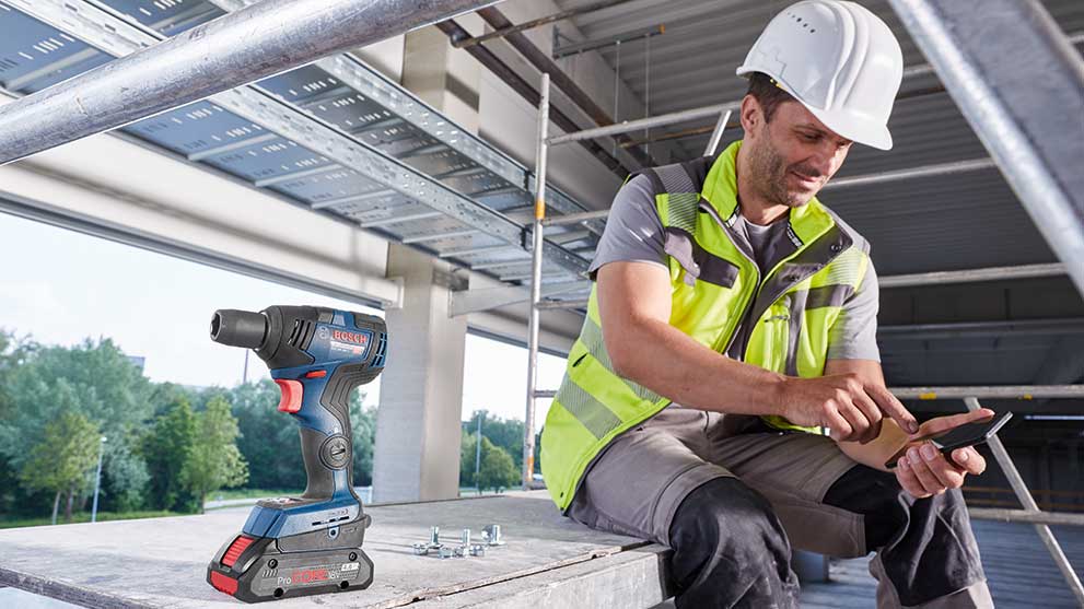 En Bosch Professional batteridrill står bredvid en byggarbetare med en telefon.