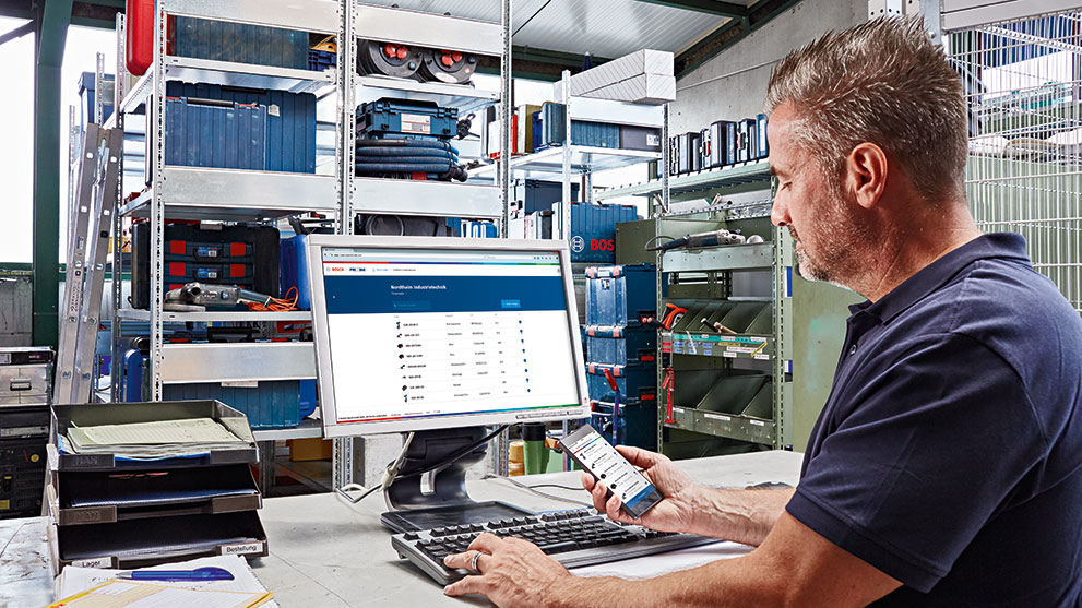 En mand bruger en computer og en smartphone i et værksted.