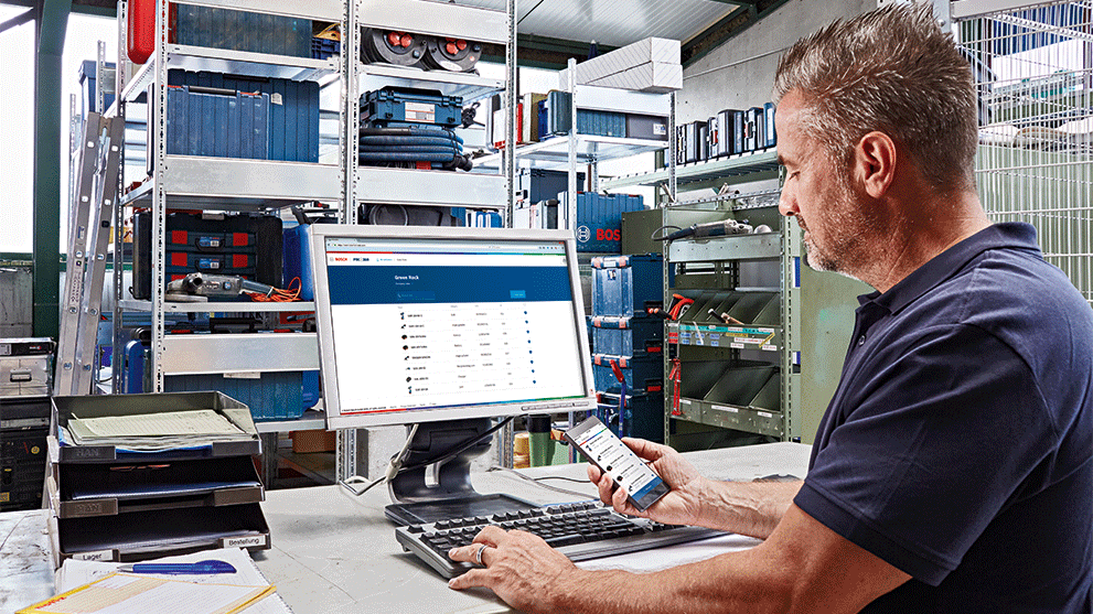 Man vid datorn med Bosch-verktyg i bakgrunden, använder smartphone.