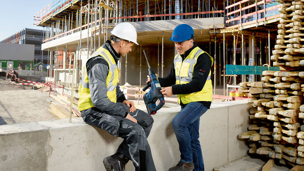 Två byggarbetare med verktyg pratar på en byggarbetsplats.