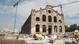 Large, unfinished building with construction cranes and construction site in the foreground.