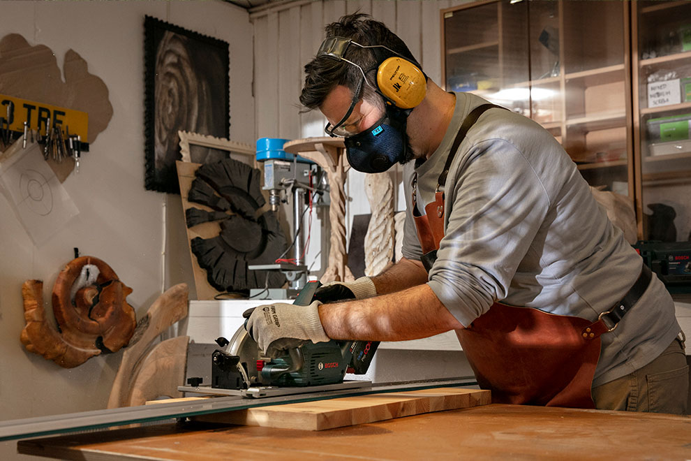 Kuulonsuojaimen käyttäjä käsityöläinen leikkaa puuta Bosch-sahalla.