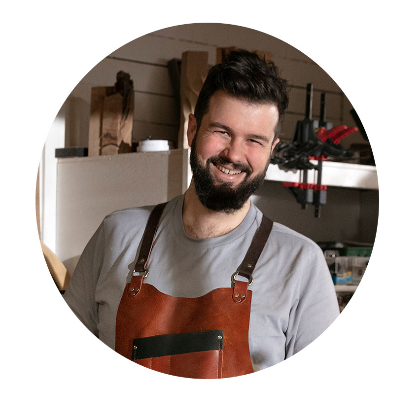 Naeratav mees nahkeseeliku sees seisab töökojas.