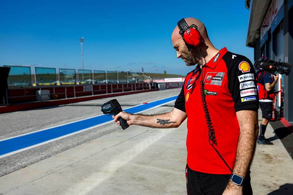 Un meccanico in camicia rossa tiene un dispositivo di misurazione su una pista da corsa.