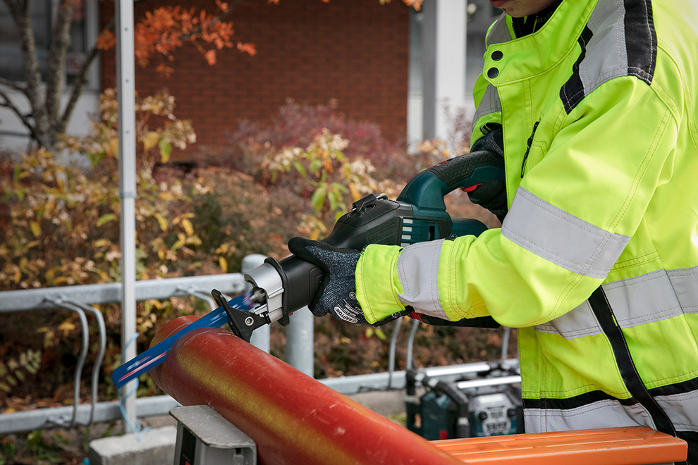 Keltapaitainen työntekijä leikkaa punaista putkea Bosch-työkalulla.