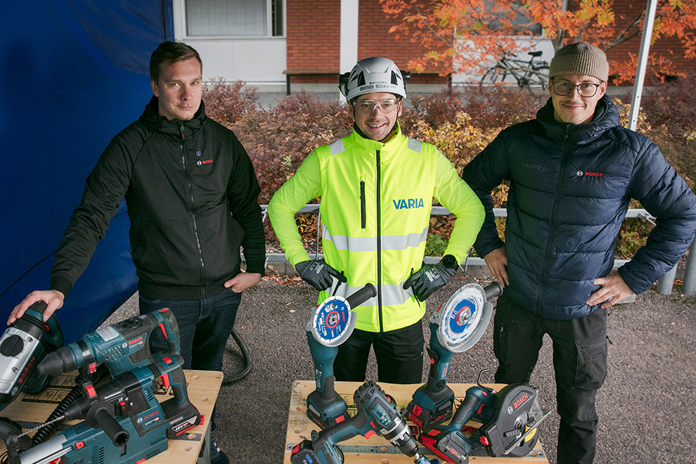 Kolme miestä seisoo Bosch-työkalujen edessä ulkona pöydän ääressä.