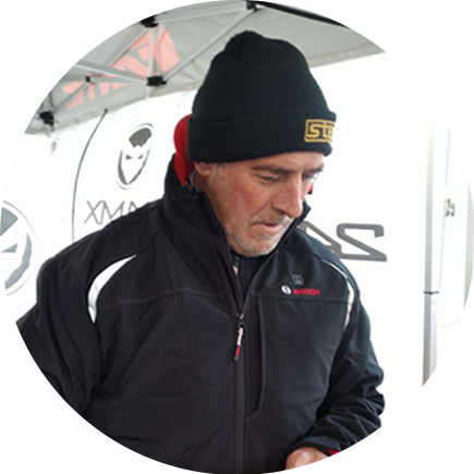 En man i svart jacka och hatt står under ett tält.